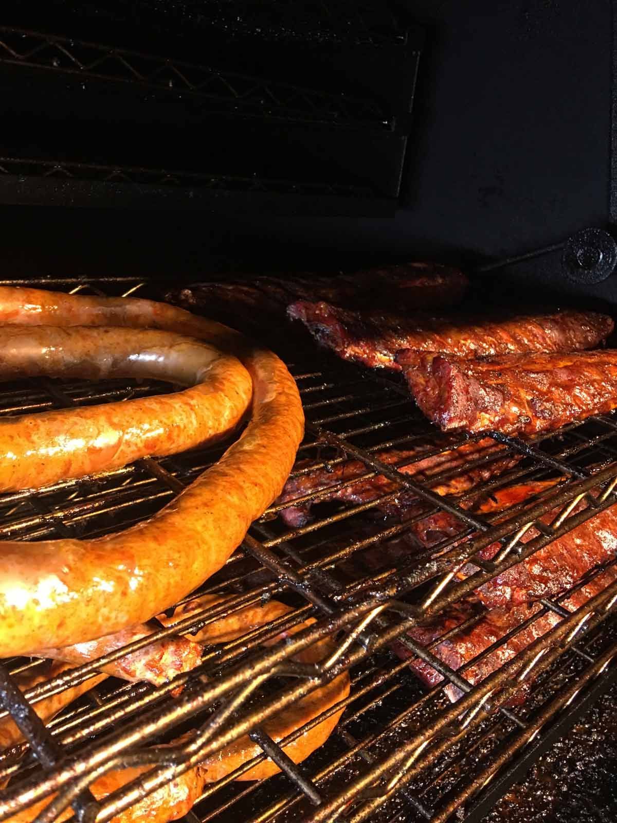 Sausages and ribs sizzling on a grill, with orange flames and charred meat close up