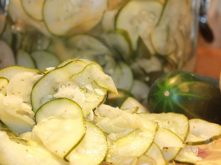 Pile of sliced cucumbers in a bowl, with a whole cucumber in the background