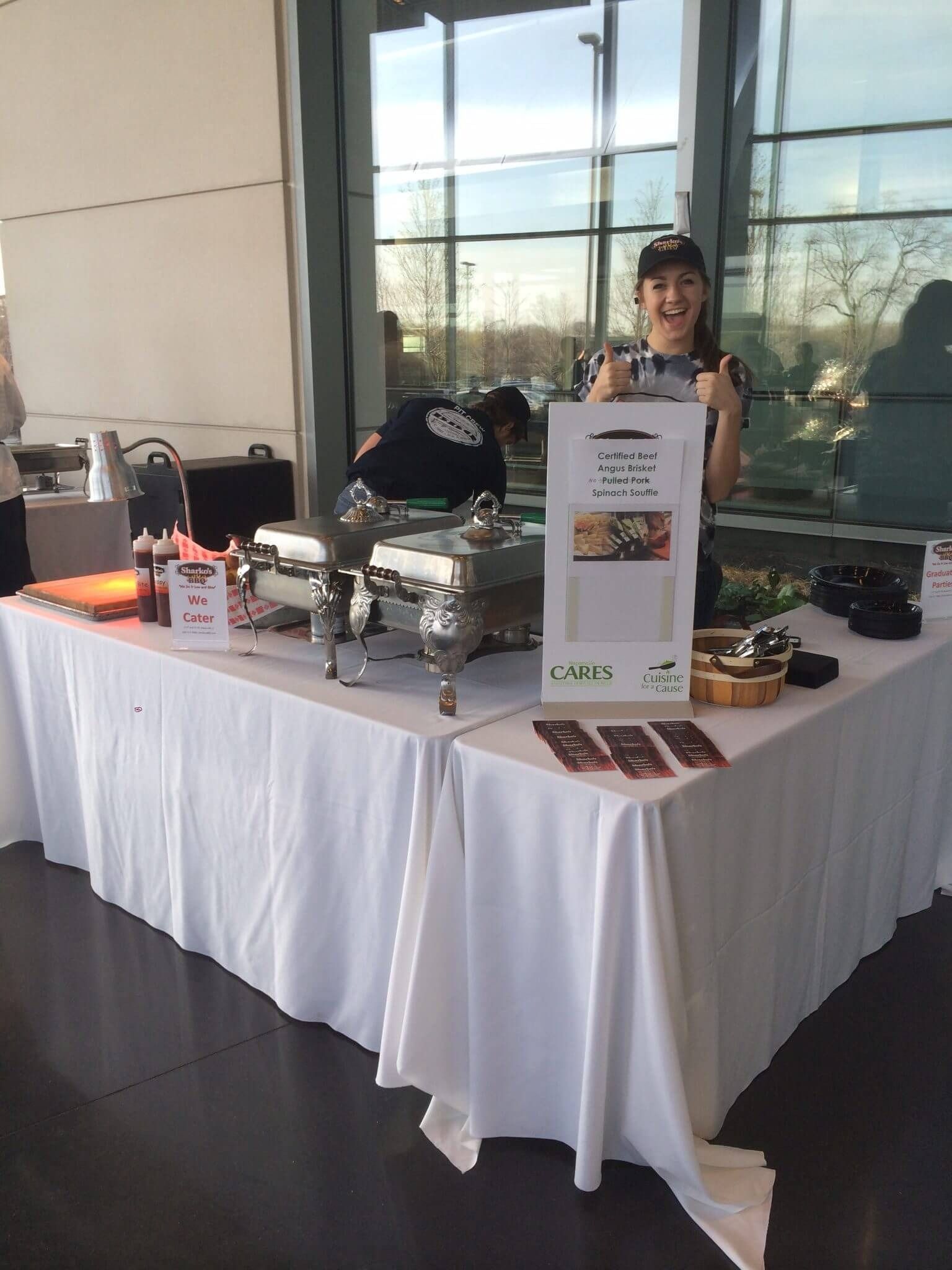 Catering table with chafing dishes and dessert display beside a person in a bright lobby