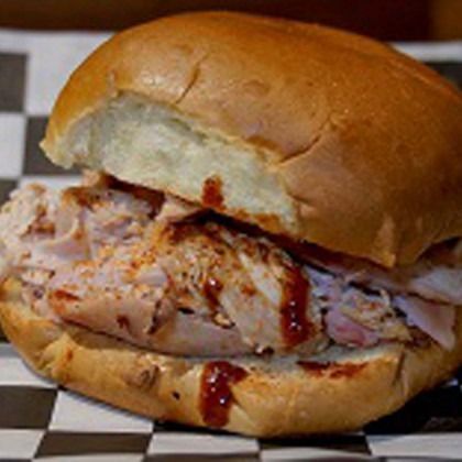Close-up of a pulled pork sandwich on a checkered tray liner, with sauce and a soft bun