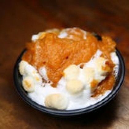 A bowl of vanilla ice cream topped with caramel sauce on a dark table