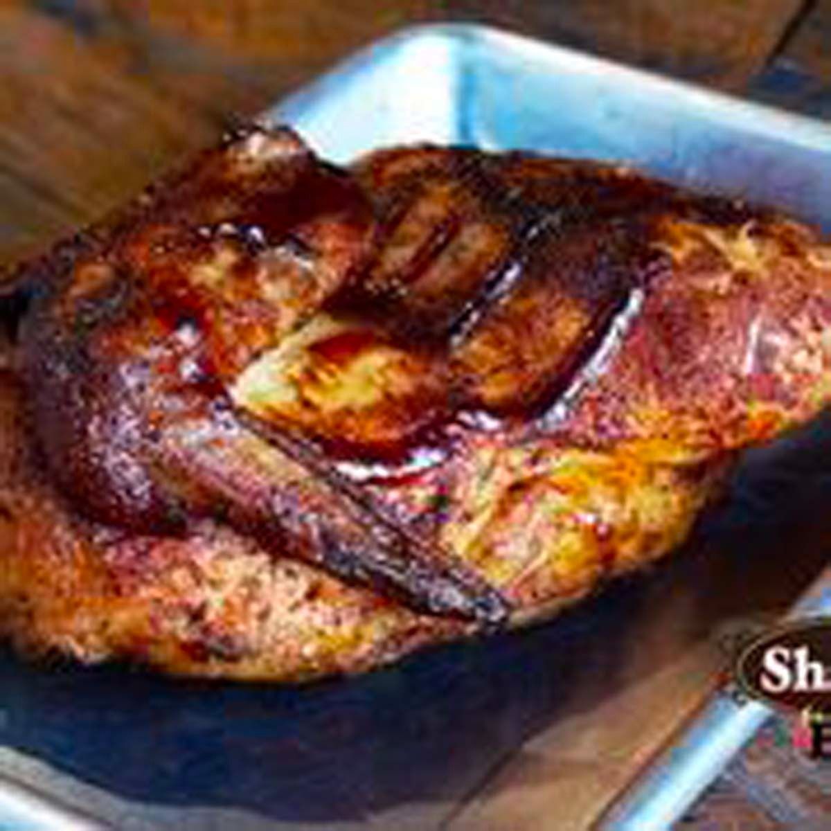 Grilled roasted meat on a tray, browned and glazed, with a dark sauce or charred surface.