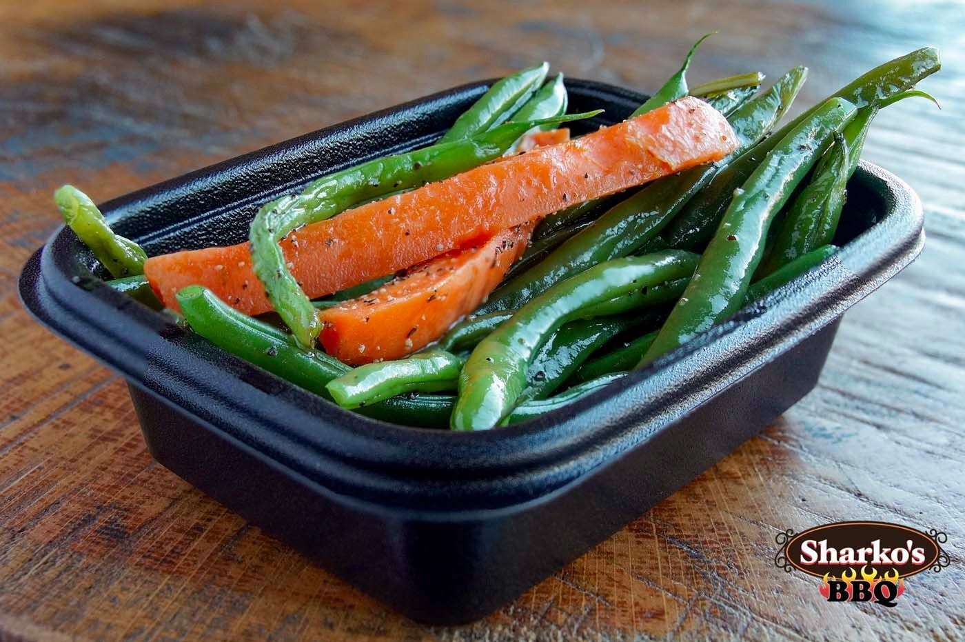 Black tray of roasted carrots and green beans on a wooden table