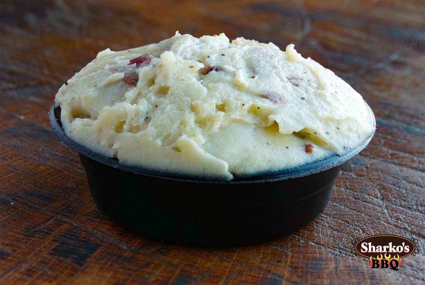 Bowl of creamy potato salad with bacon bits on a wooden table