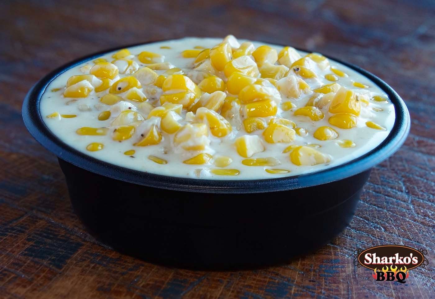 Black bowl of creamy corn pudding topped with yellow corn kernels on a wooden table