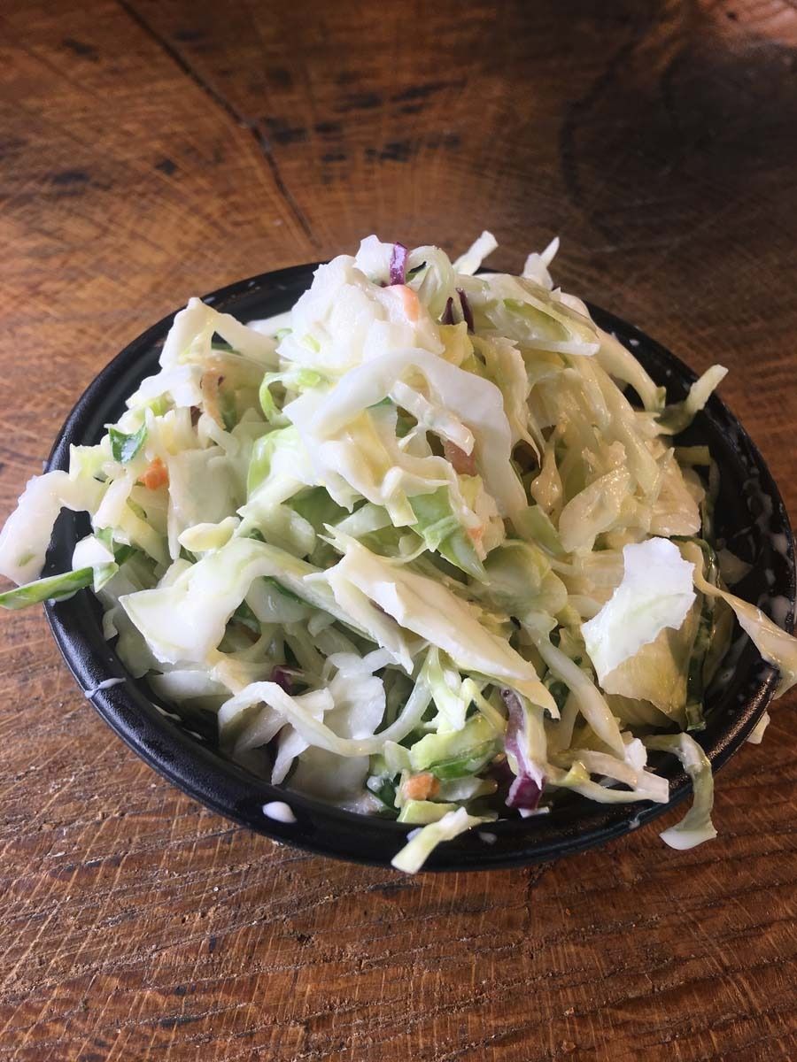 Small bowl of shredded cabbage salad with green herbs on a wooden table