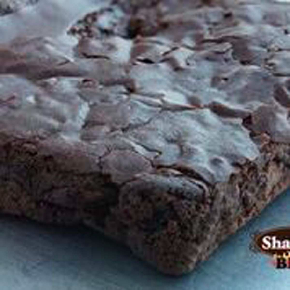 Close-up of a chocolate brownie with a crinkled, powdered top on a white surface.