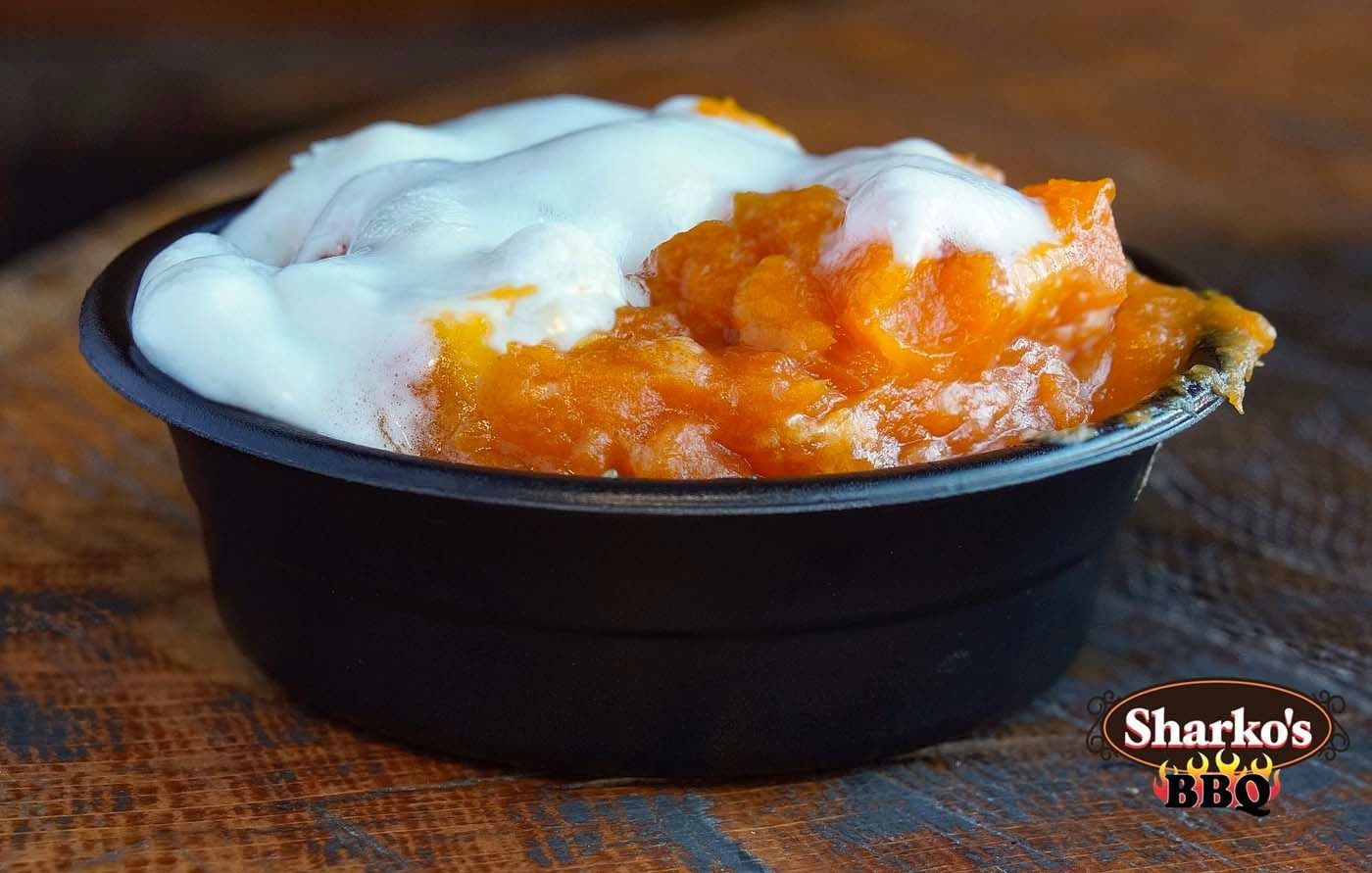 Black bowl of orange dessert topped with whipped cream on a wooden table