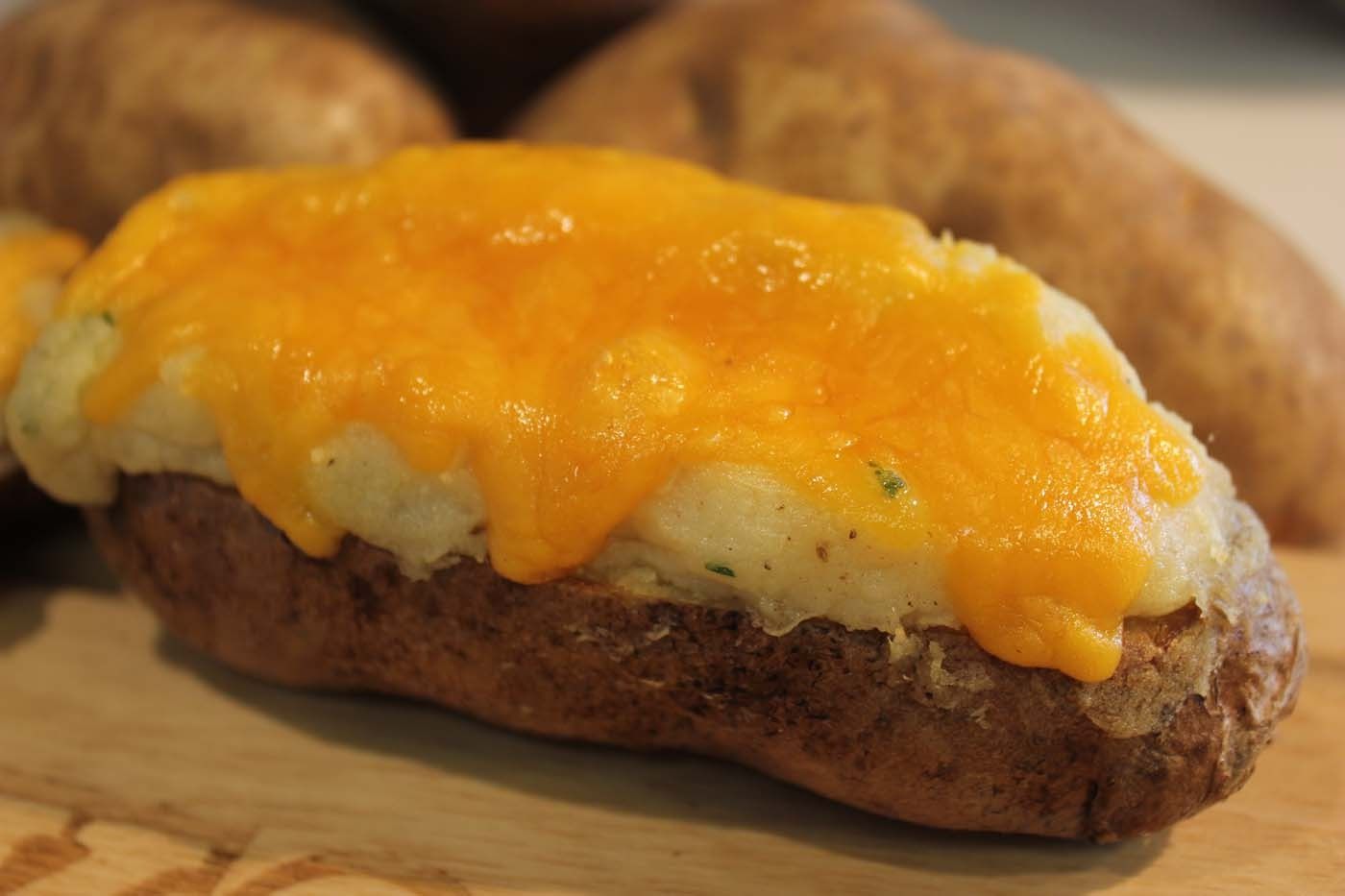 Baked potato topped with melted cheddar cheese on a cutting board