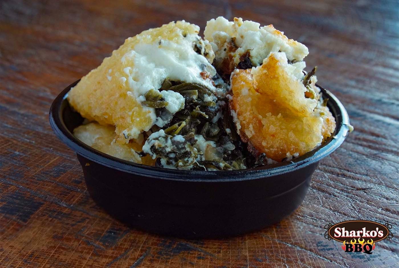 A black bowl of BBQ topped with crumbly cornbread on a wooden table