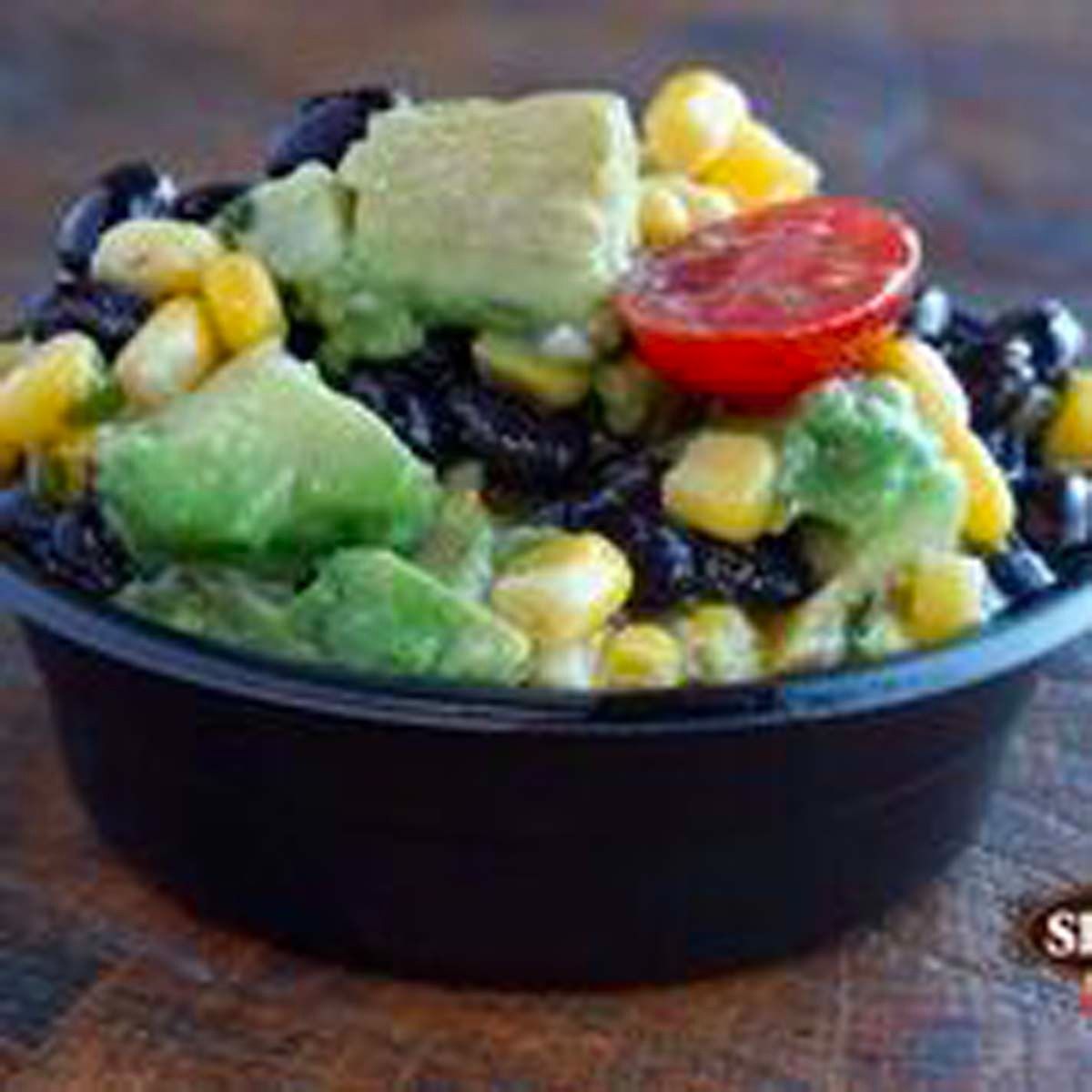 Black bowl of colorful salad with avocado, black beans, corn, and cherry tomatoes