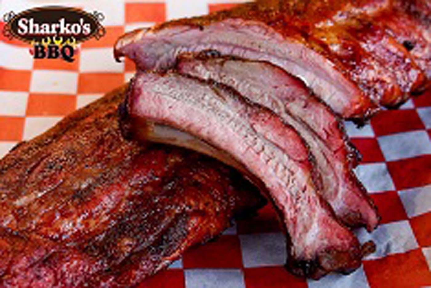 Sliced smoked ribs on red-and-white checkered paper with Sharko’s BBQ logo