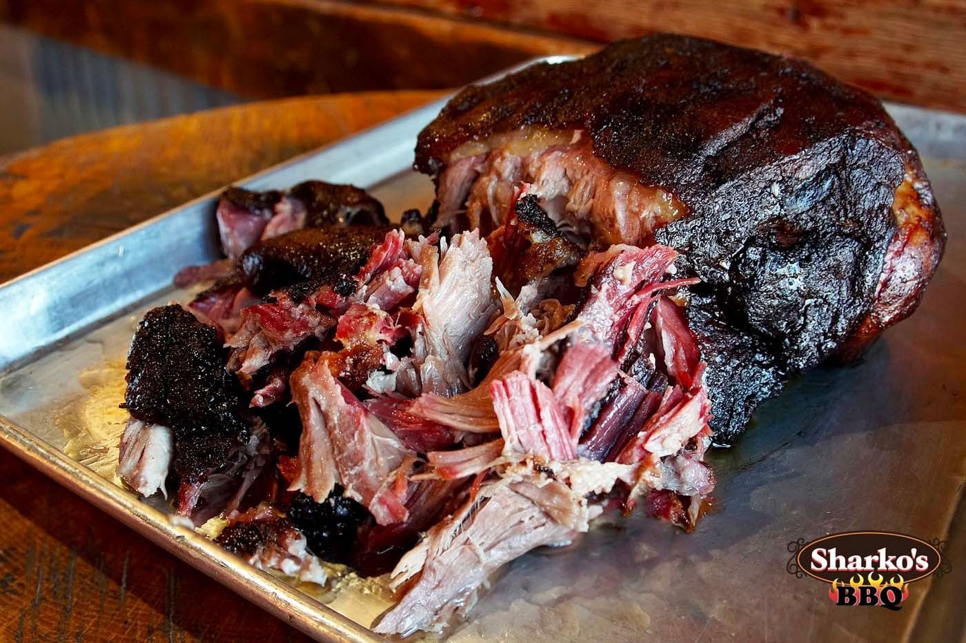 Barbecue pulled pork on a metal tray, with dark bark and shredded meat in a close-up
