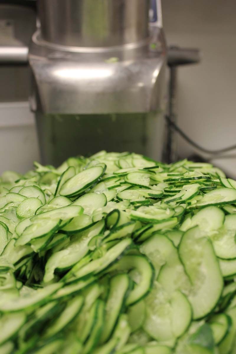 Sliced cucumbers piled in a stainless steel kitchen machine