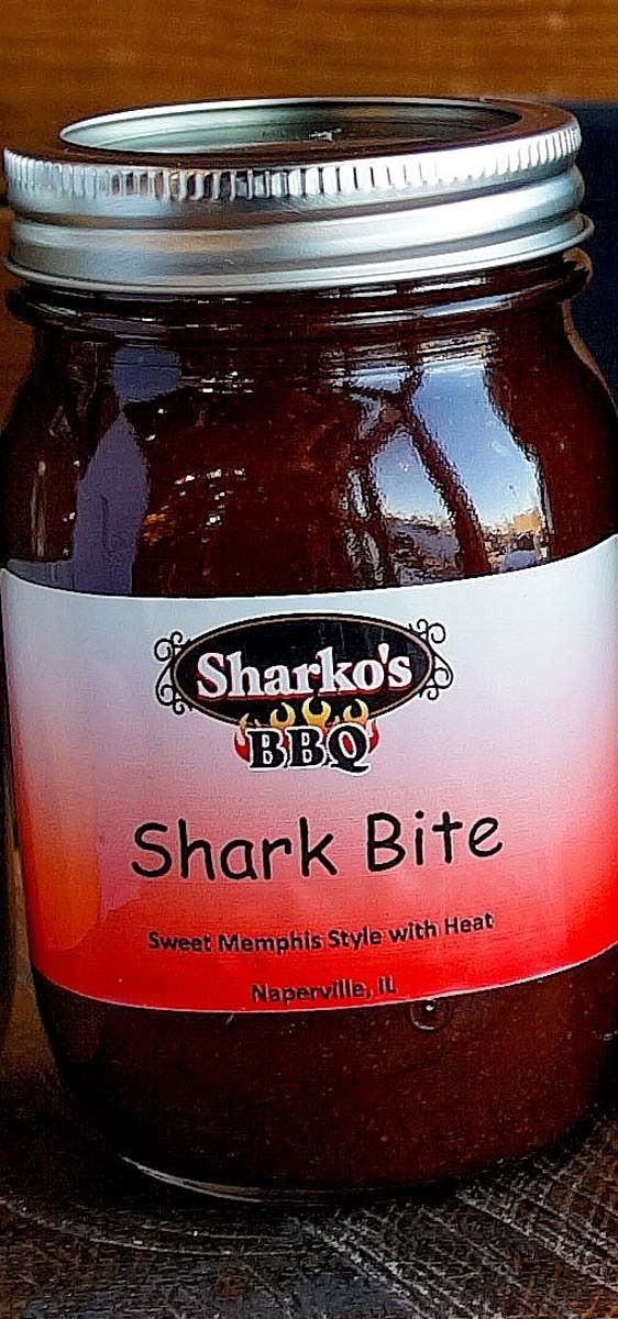 Jar of Shark Bite sauce with a red label and silver lid on a wooden surface.