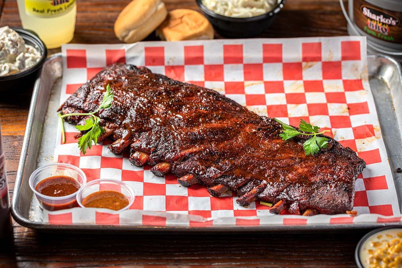 Barbecue ribs glazed with sauce on a red-and-white checkered tray, with dipping sauce on the side