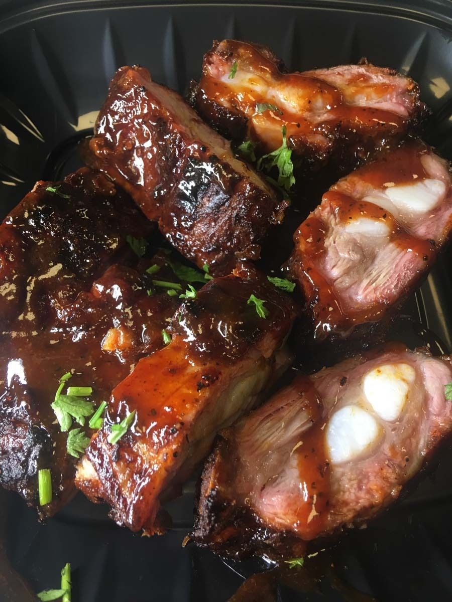 Glazed barbecue ribs in a black tray, topped with chopped green herbs