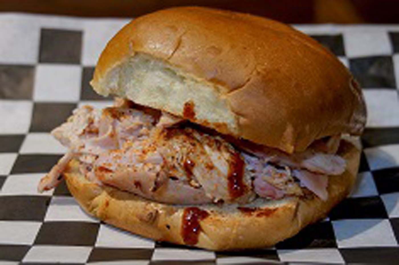 Pulled pork sandwich with barbecue sauce on checkered paper.