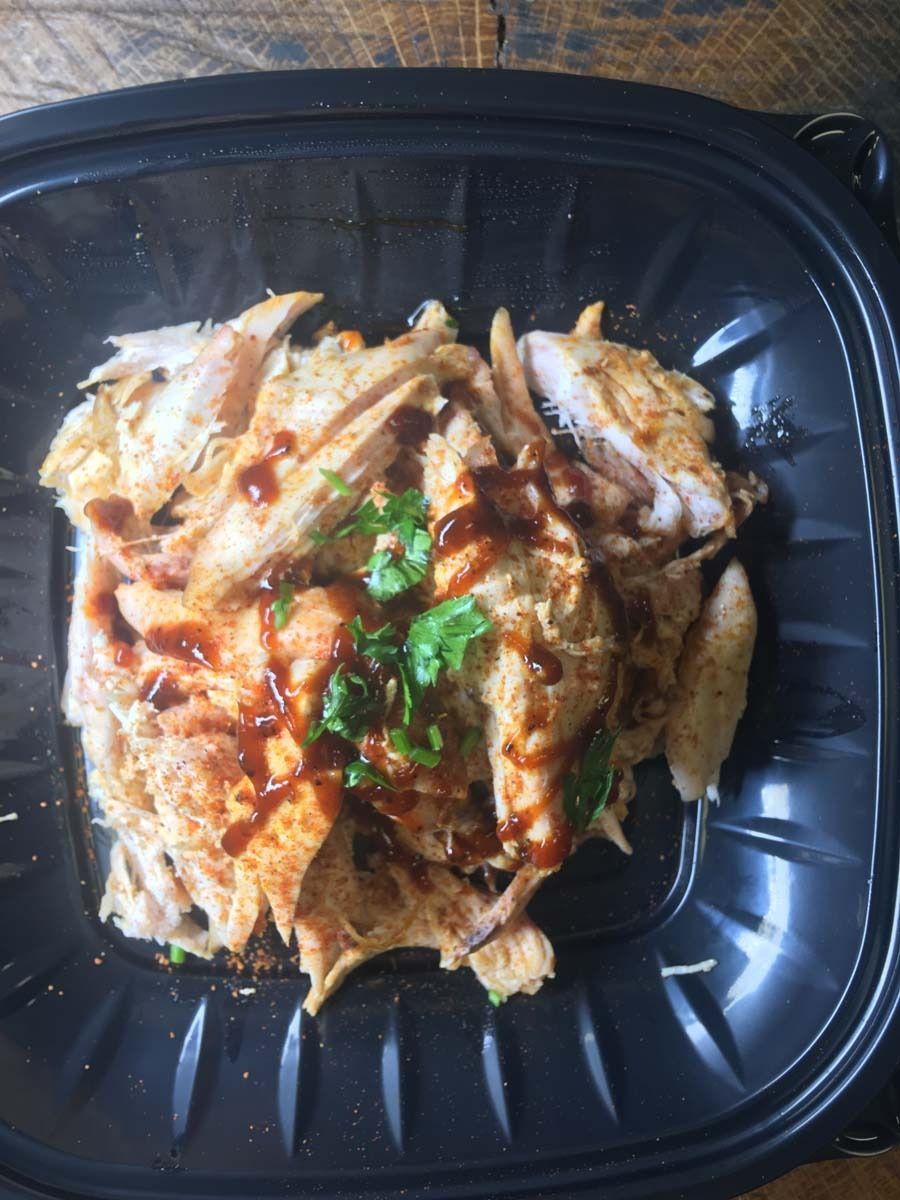 Saucy shredded chicken topped with cilantro in a black plastic takeout container