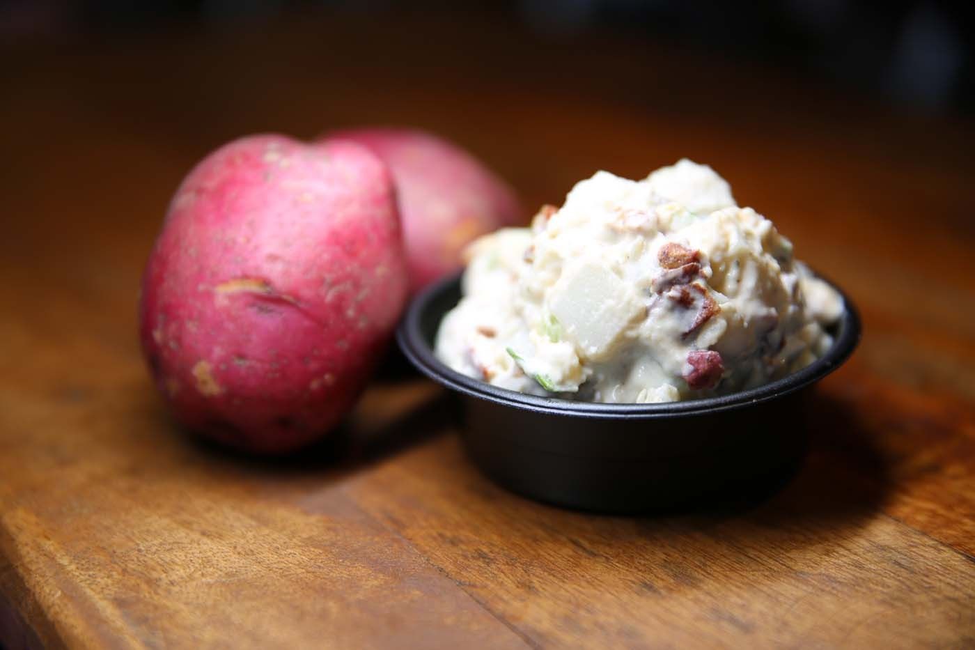 Two red potatoes beside a bowl of mashed potatoes on a wooden table