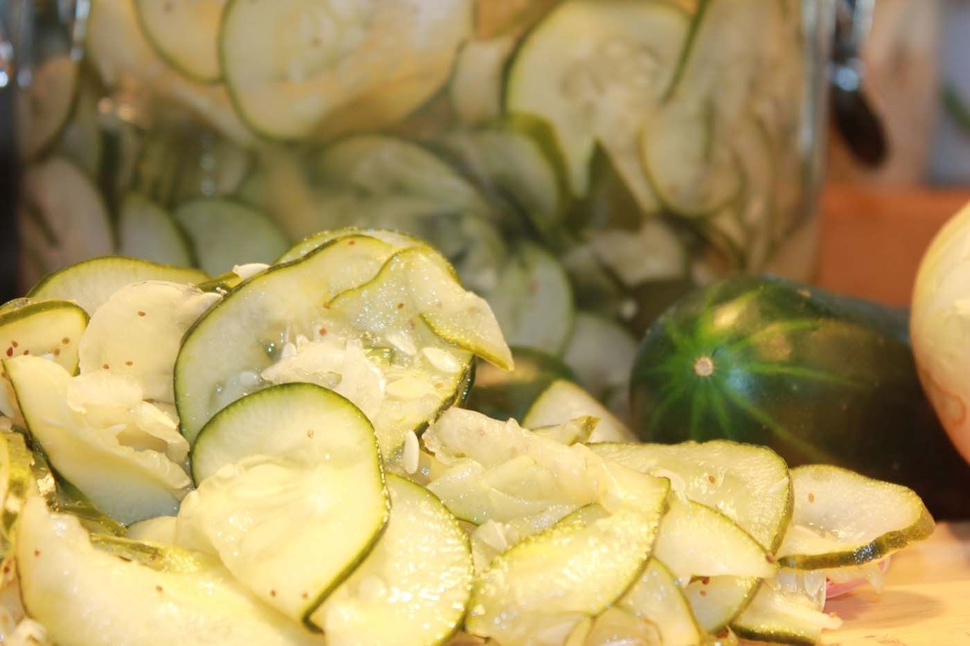 Sliced cucumbers and a jar of pickled cucumber slices on a countertop