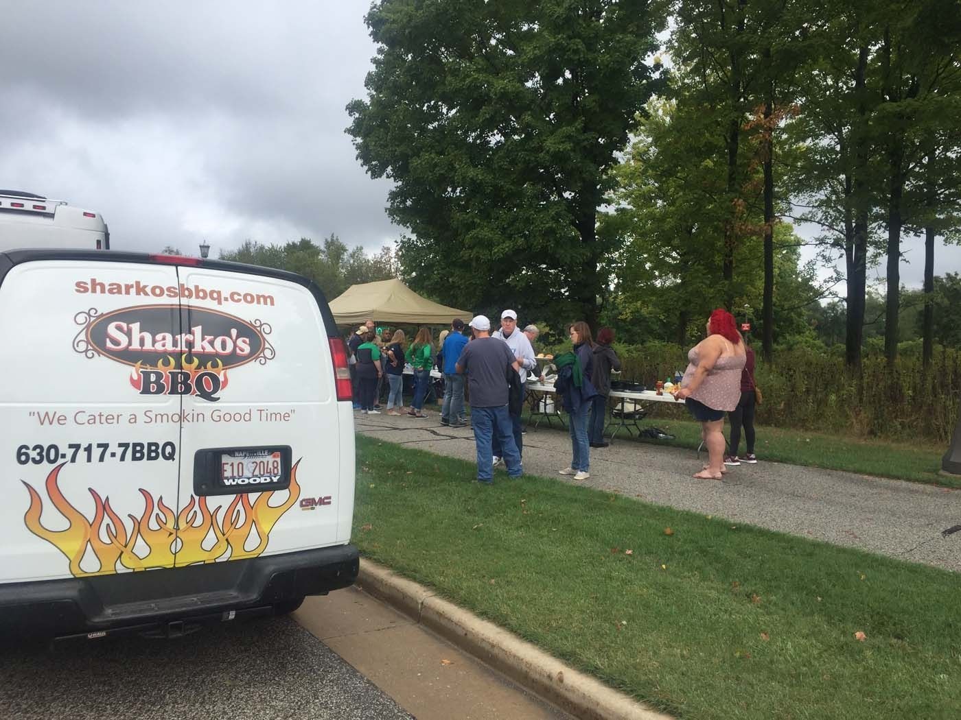 Sharko’s BBQ catering truck beside people gathered under tents in a park area