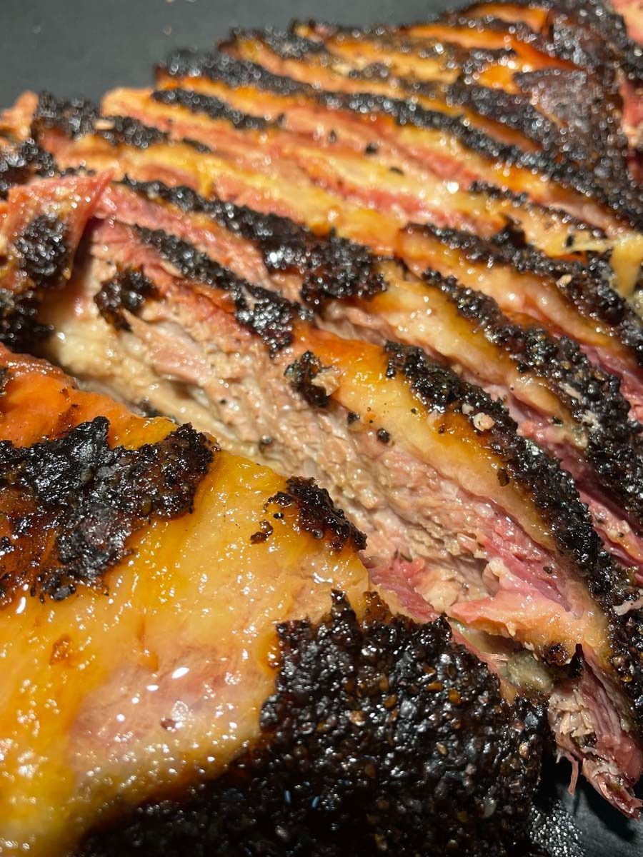 Close-up of grilled meat with dark charred crust and pink center, sliced to reveal juicy layers