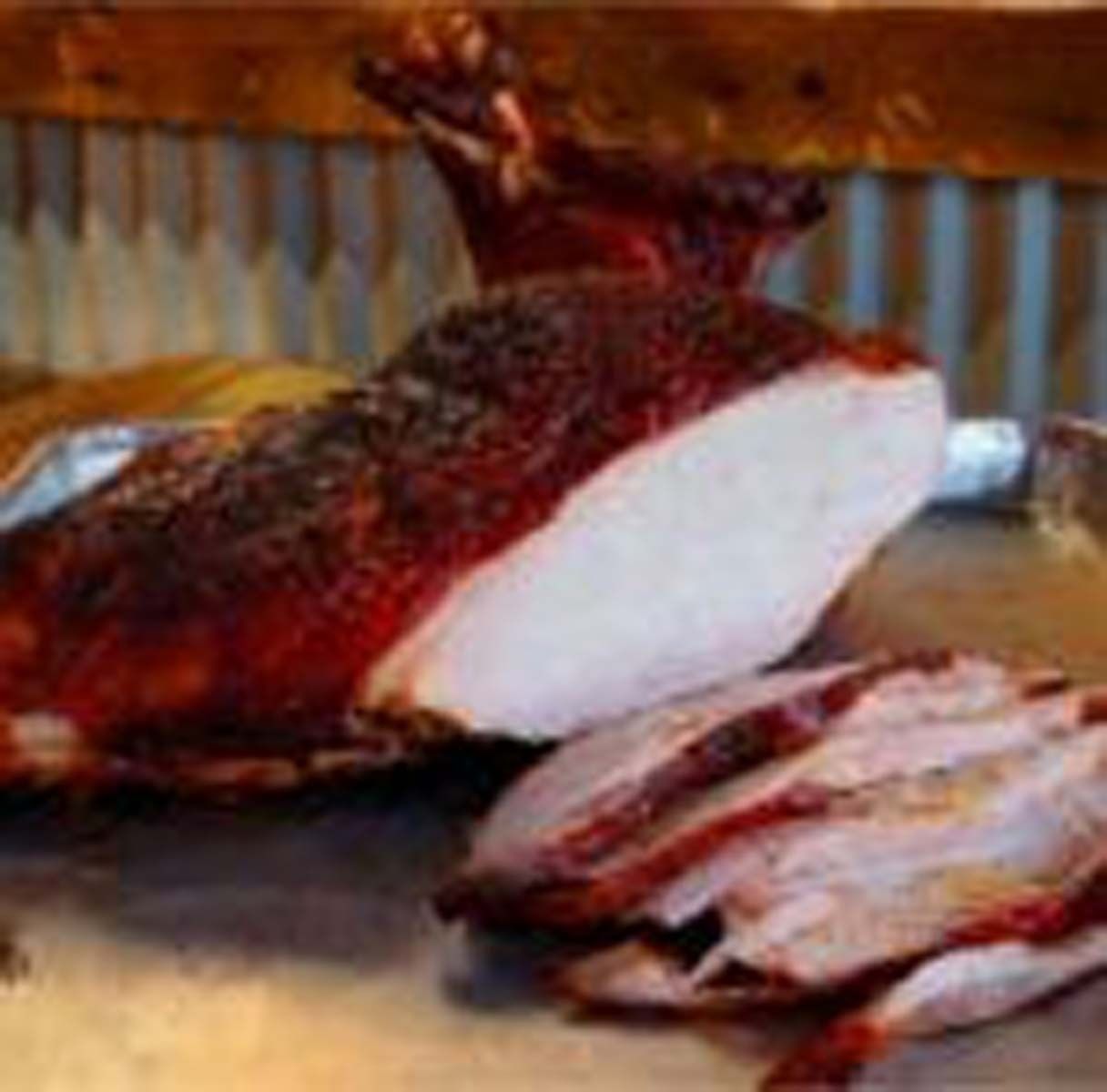 Sliced smoked roast on a tray, with a large piece of meat showing a dark crust and white interior.