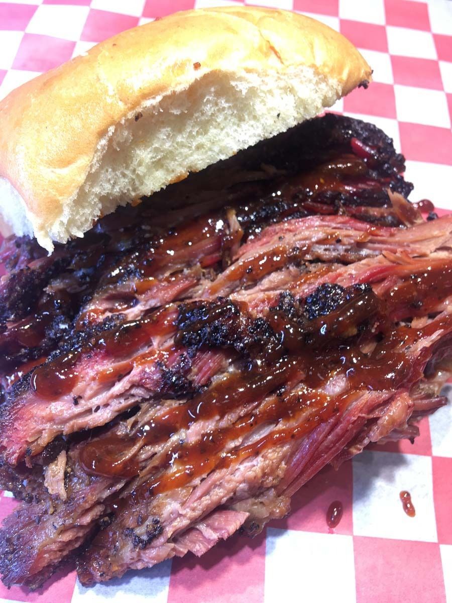 Pulled pork sandwich on a bun with smoky, sauced meat on red-and-white paper
