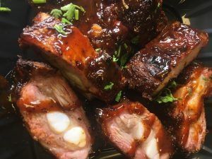Glazed grilled meat pieces garnished with chopped herbs on a dark plate