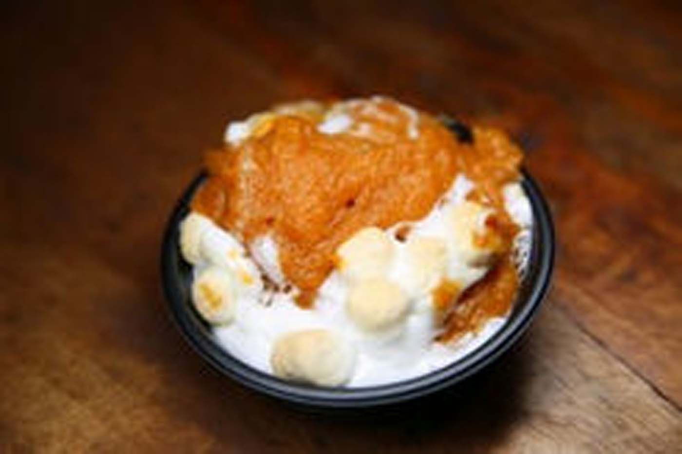 Bowl of shaved ice topped with orange syrup and white mochi balls on a wooden table