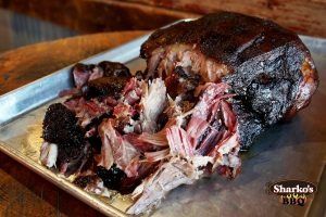 Smoked pulled pork on a metal tray, with dark bark and shredded meat visible.