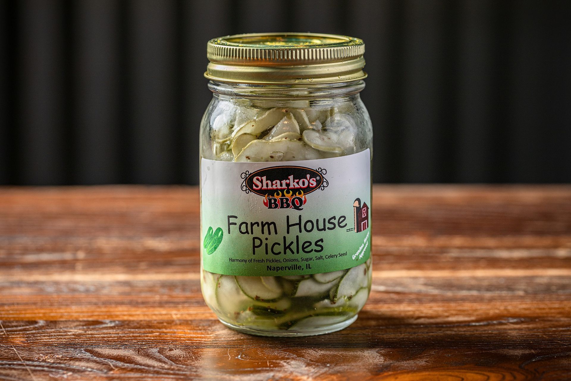 Jar of Farm House Pickles with a gold lid on a wooden table, against a dark background