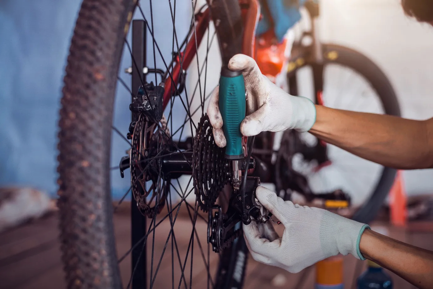 Person in gloves uses a screwdriver on a bicycle's gears.