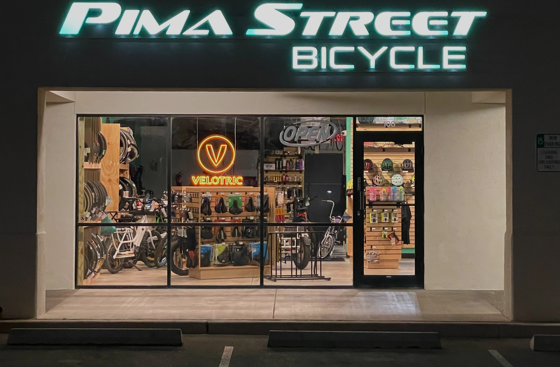 Pima Street Bicycle shop storefront at night with bright neon sign and bikes visible inside
