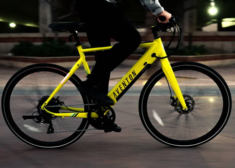 Yellow Aventon e-bike with rider on a paved road at night; bike frame reads