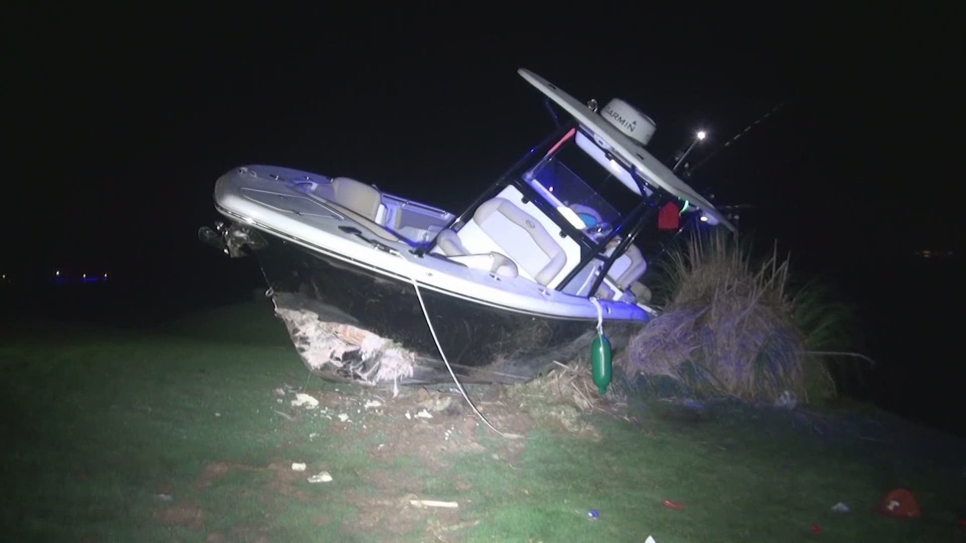 Boat tilted in shallow water at night, spotlighted near the shore with debris nearby.