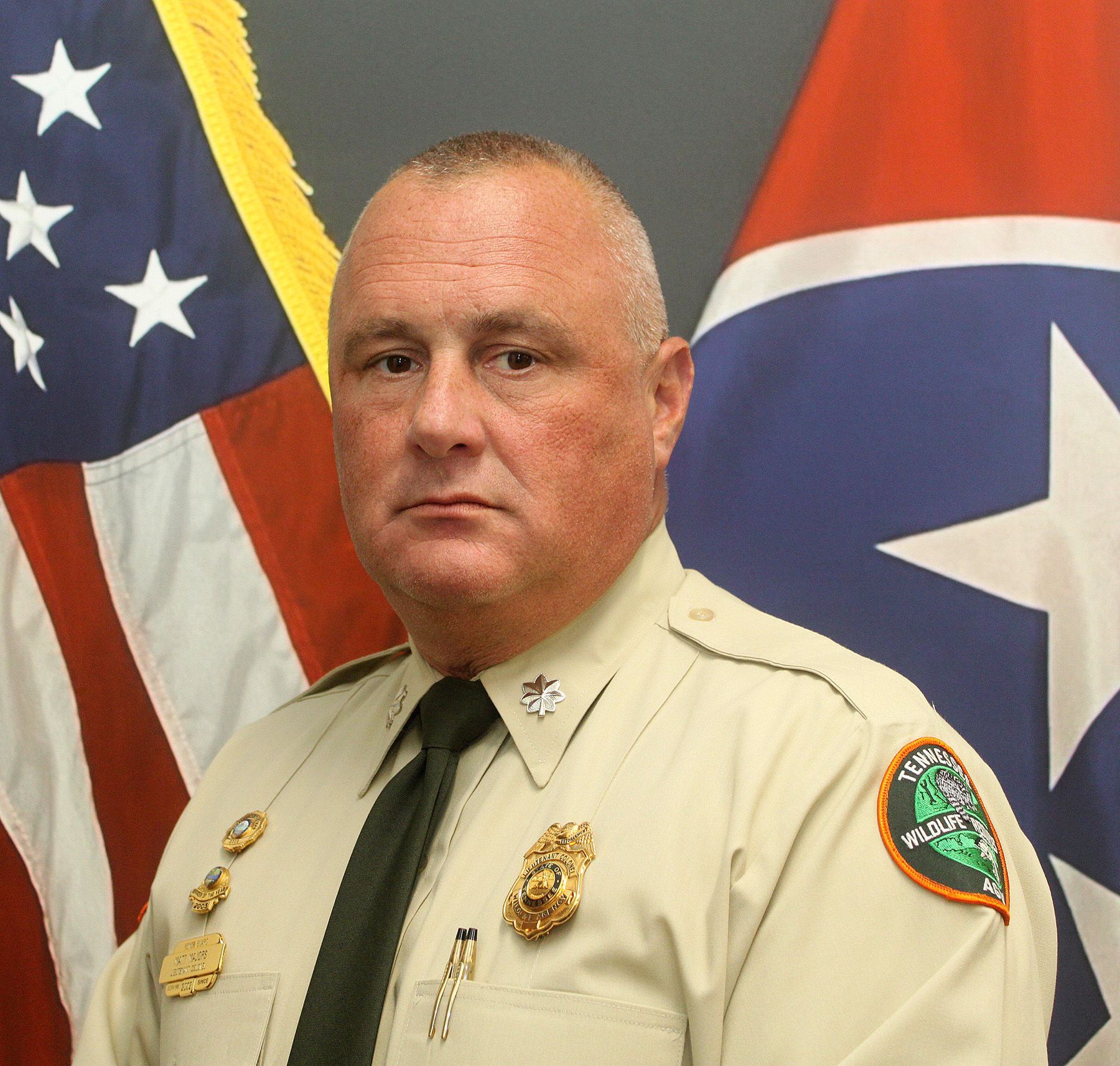 Sheriff in tan uniform standing before U.S. and Tennessee flags
