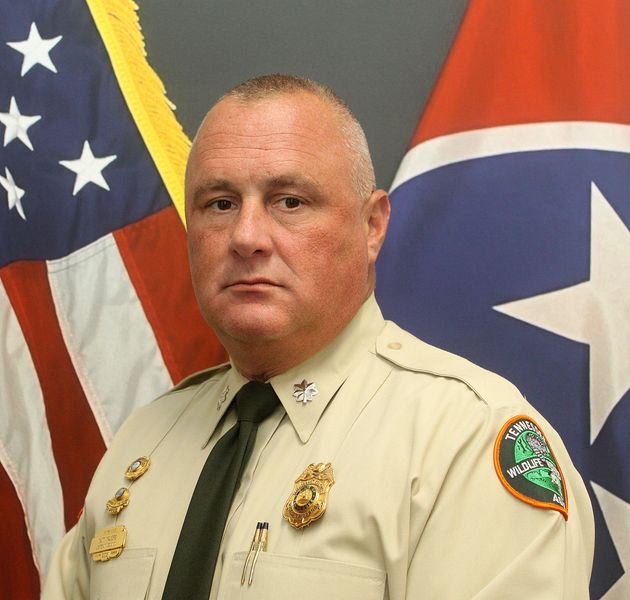 Uniformed officer standing before U.S. and Tennessee flags
