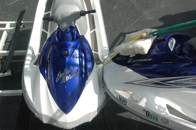 Two jet skis on choppy blue water under a cloudy sky, one gray with a rider and one blue behind it
