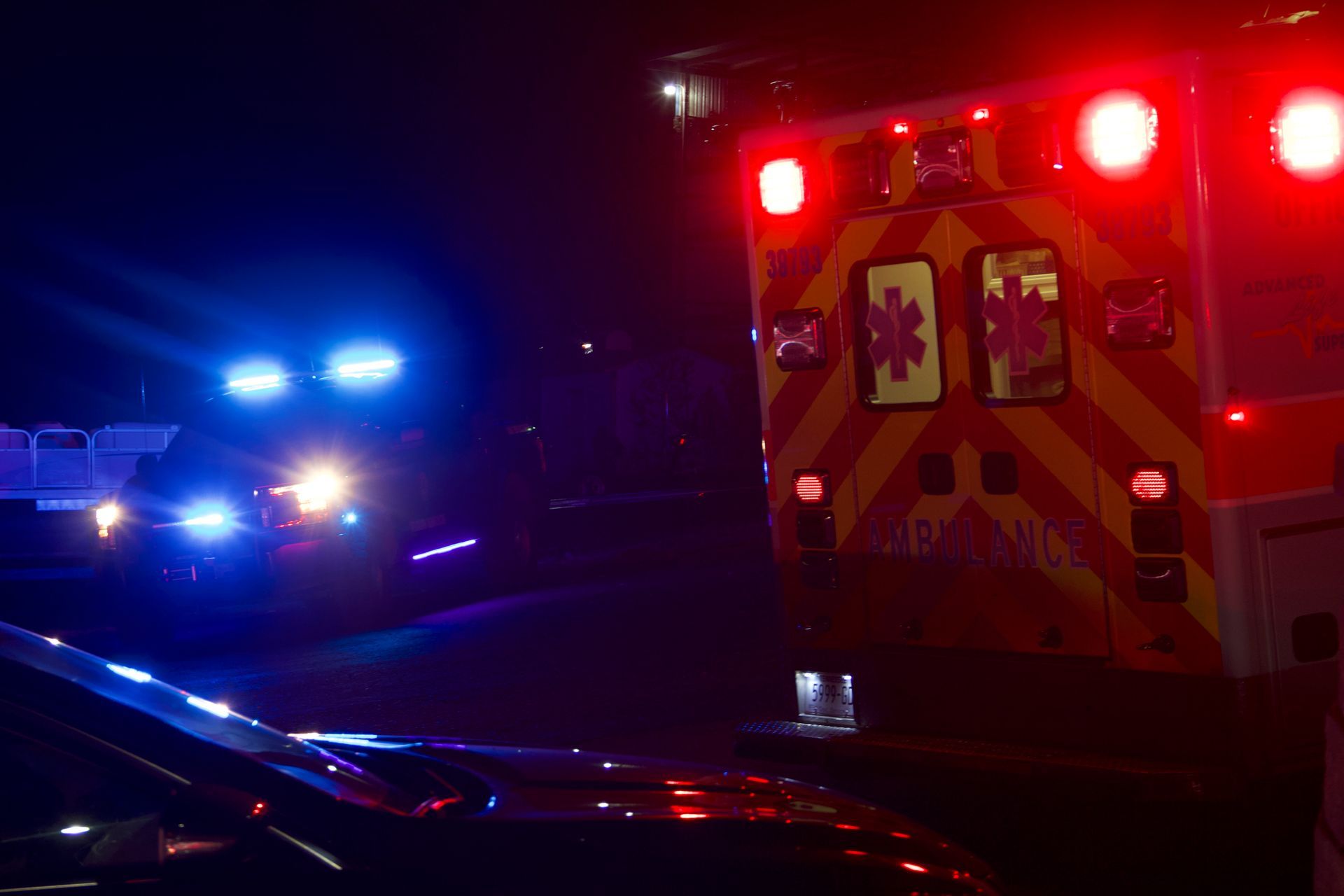 Night emergency scene with flashing police and ambulance lights on a dark road