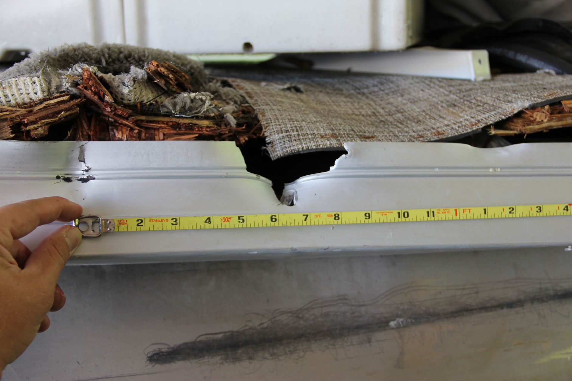 Hand measuring a damaged, torn boat section with a tape measure and exposed debris
