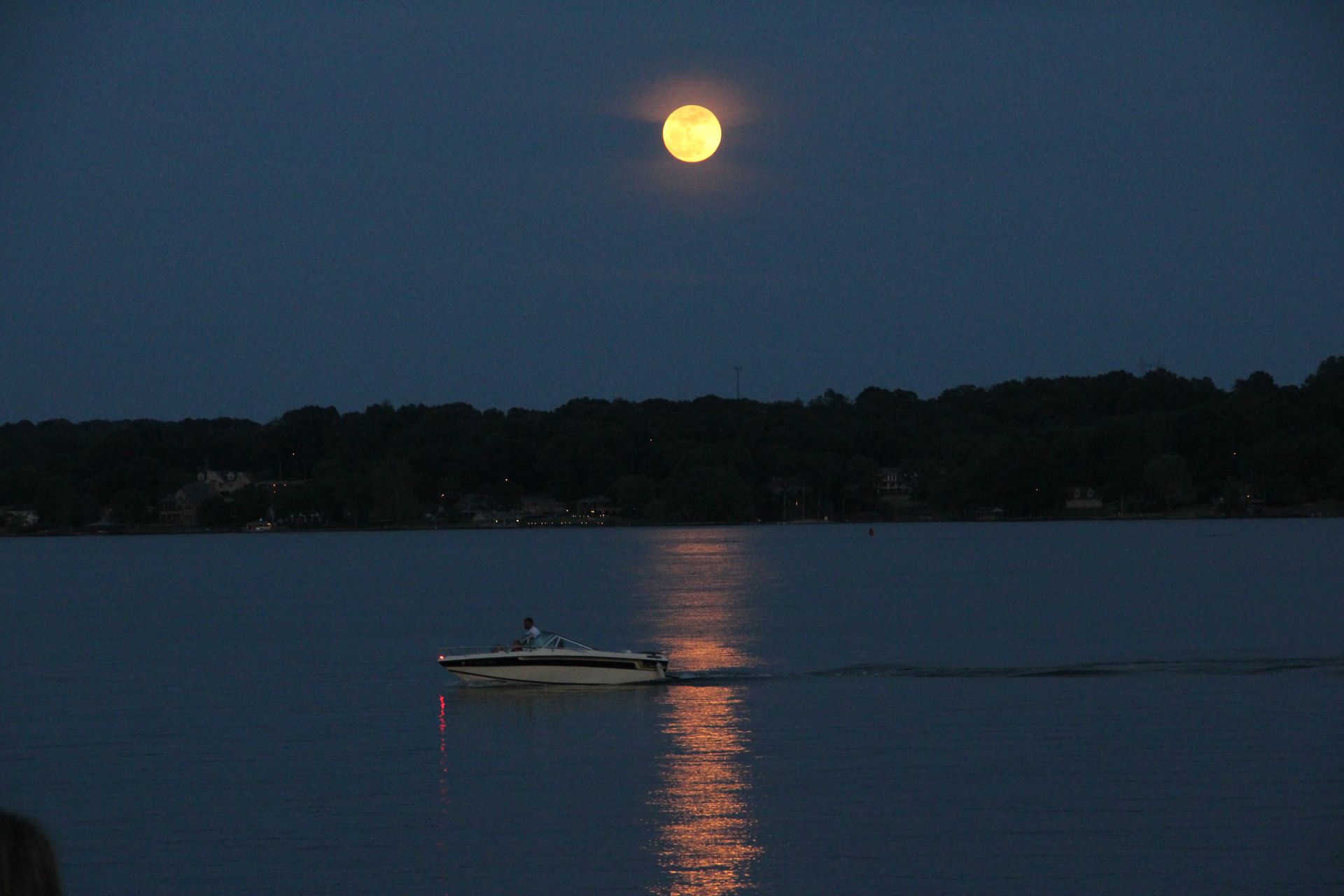Moonlit lake with a small boat leaving a reflection on the water at dusk