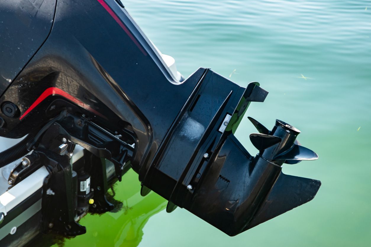 Close-up of a black outboard motor mounted on a boat, with green water in the background