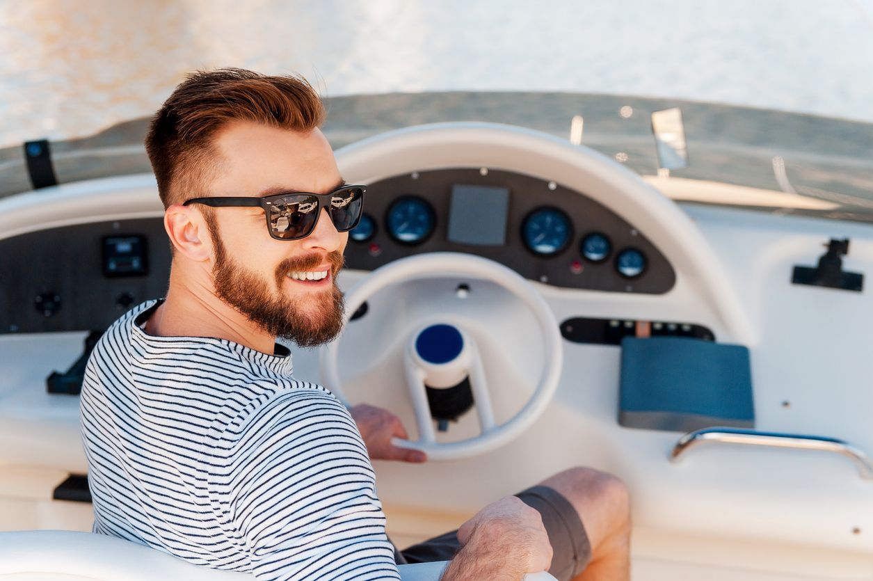 Smiling man in sunglasses steering a boat cockpit on the water