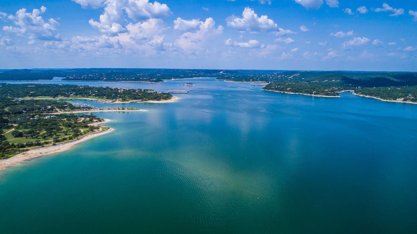 Aerial view of a wide blue lake with green shores and a partly cloudy sky