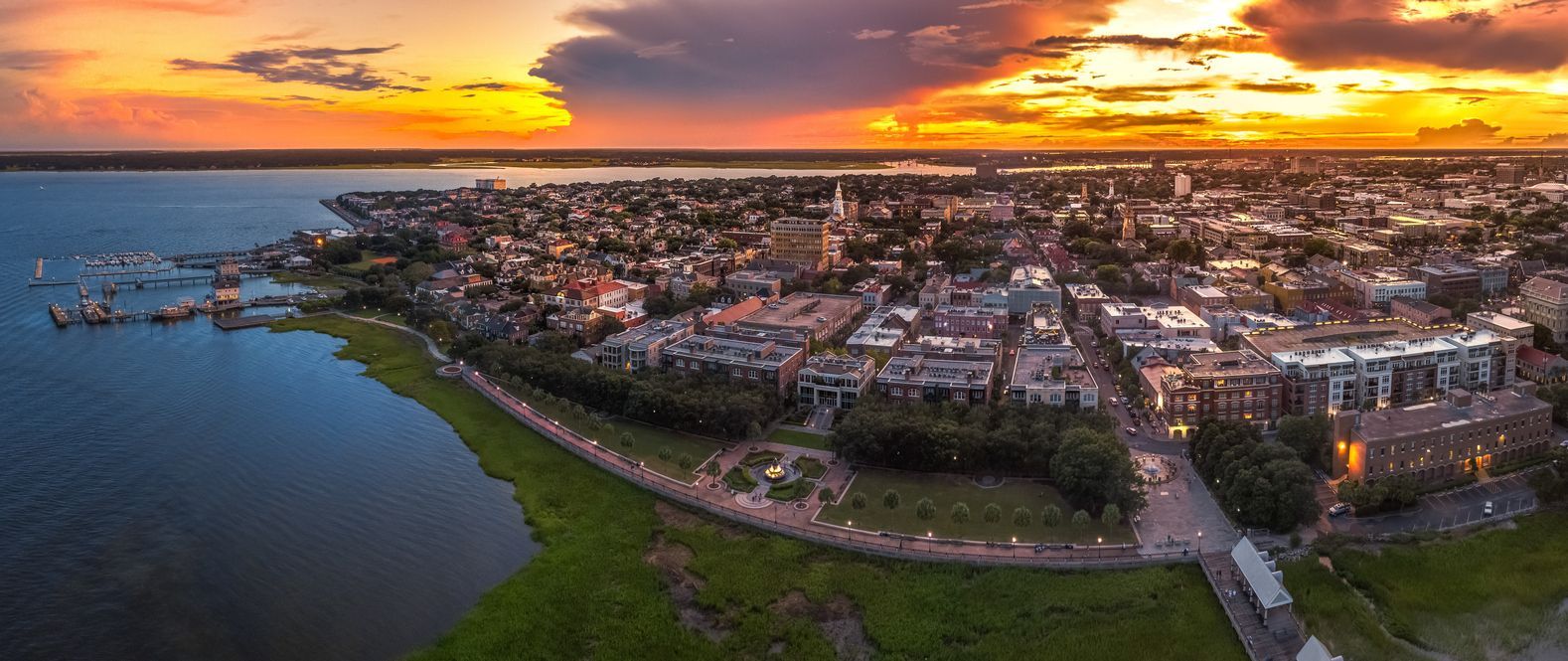 Aerial sunset view of a coastal city with water, shoreline, and glowing orange sky