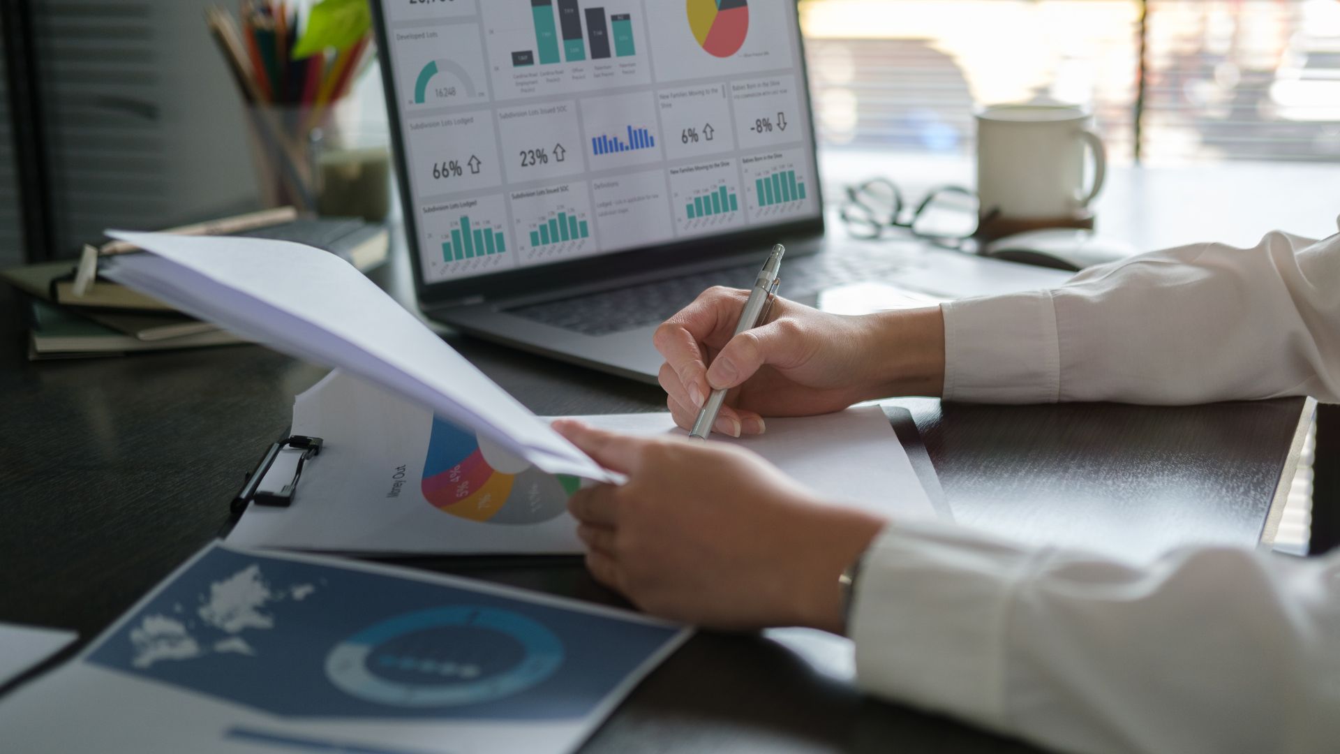 Persona che scrive documenti e analizza grafici sul computer portatile in uno spazio di lavoro.