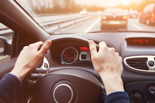 Hands gripping a steering wheel, driving on a highway with other cars, sunny day. | Dave's Automotive LLC