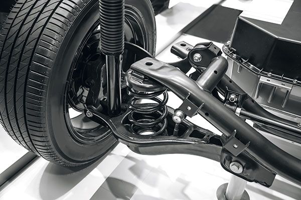 Black and white close-up of car suspension system: tire, coil spring, shock absorber, and control arms. | Dave's Automotive LLC